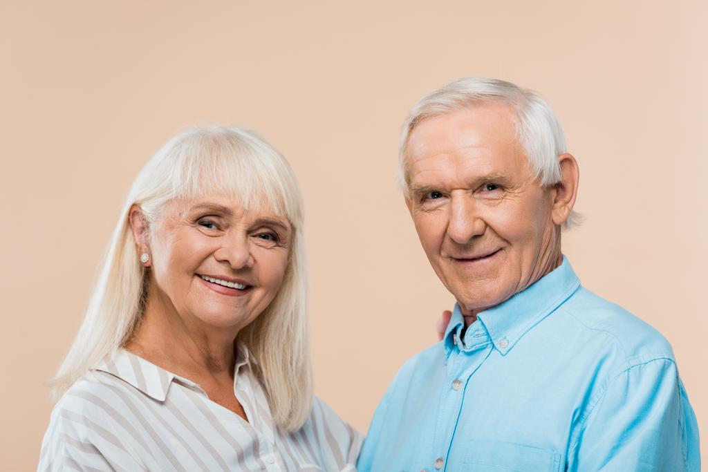 glückliches Rentnerehepaar mit grauen Haaren, das vereinzelt auf beige gekleidet in die Kamera blickt  - Foto, Bild