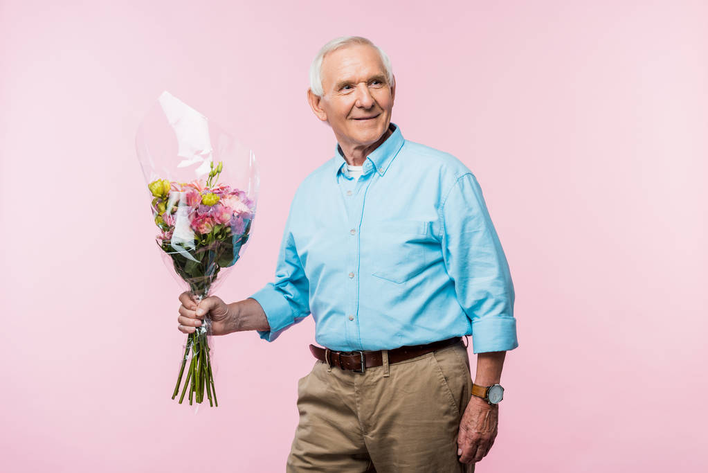 χαρούμενος ανώτερος άνθρωπος κρατώντας μπουκέτο λουλουδιών, ενώ στέκεται σε ροζ  - Φωτογραφία, εικόνα
