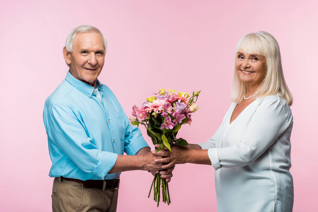 Veselý starší muž dávící kytici květinami do šťastné manželky v důchodu na růžovém  - Fotografie, Obrázek