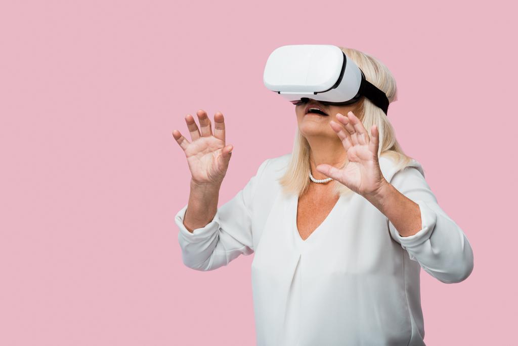 donna in pensione gesticolare mentre indossa auricolare realtà virtuale isolato su rosa
  - Foto, immagini