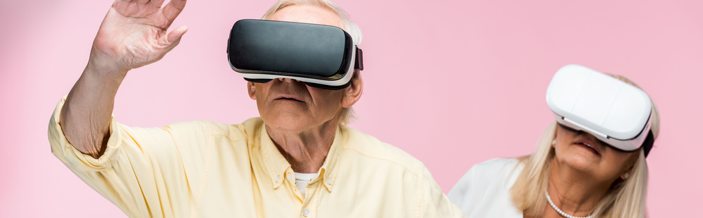 panoramische foto van gepensioneerde man gebaren terwijl het dragen van Virtual Reality headset in de buurt van vrouw op roze  - Foto, afbeelding