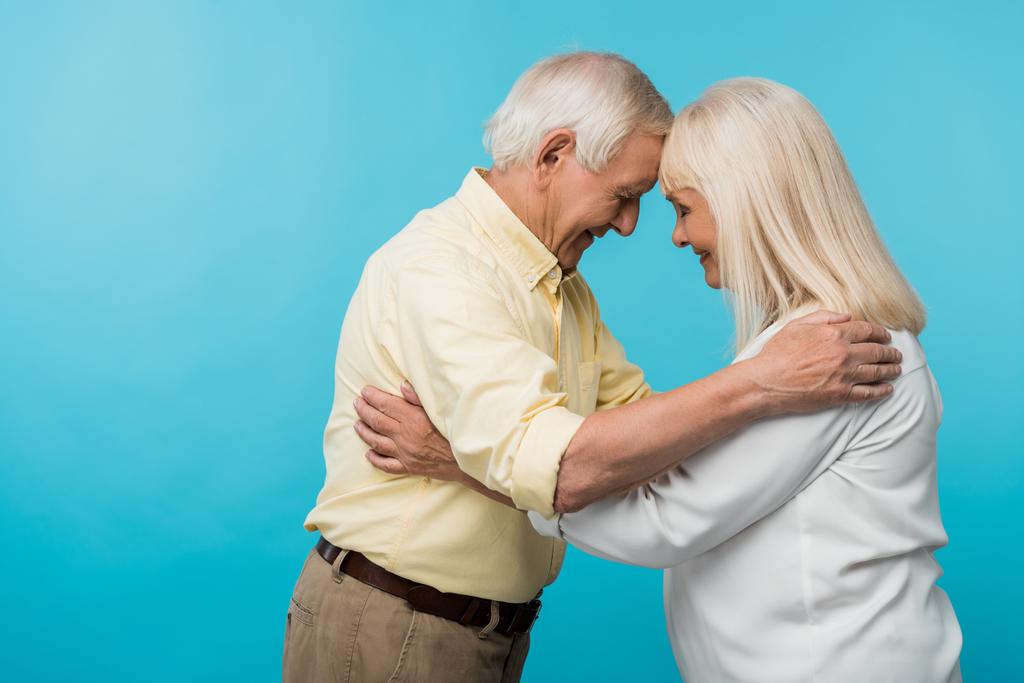 Widok z boku wesołej emerytowanej pary z zamkniętymi oczami uśmiechniętymi na niebiesko  - Zdjęcie, obraz