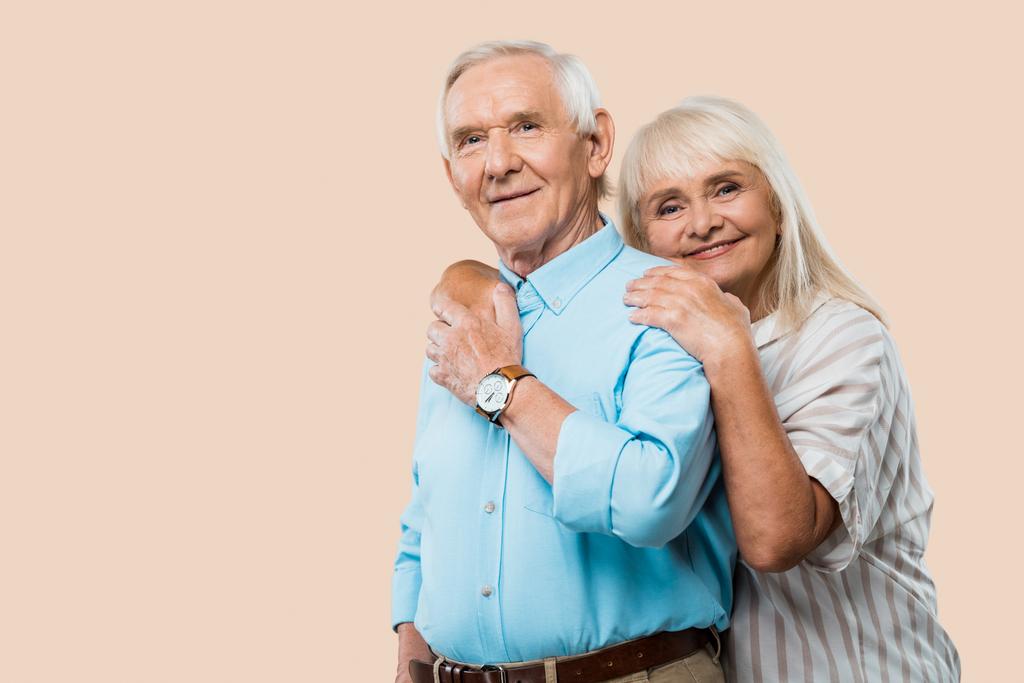 χαρούμενη συνταξιούχος γυναίκα αγκαλιάζει ανώτερος σύζυγος απομονώνεται σε μπεζ  - Φωτογραφία, εικόνα