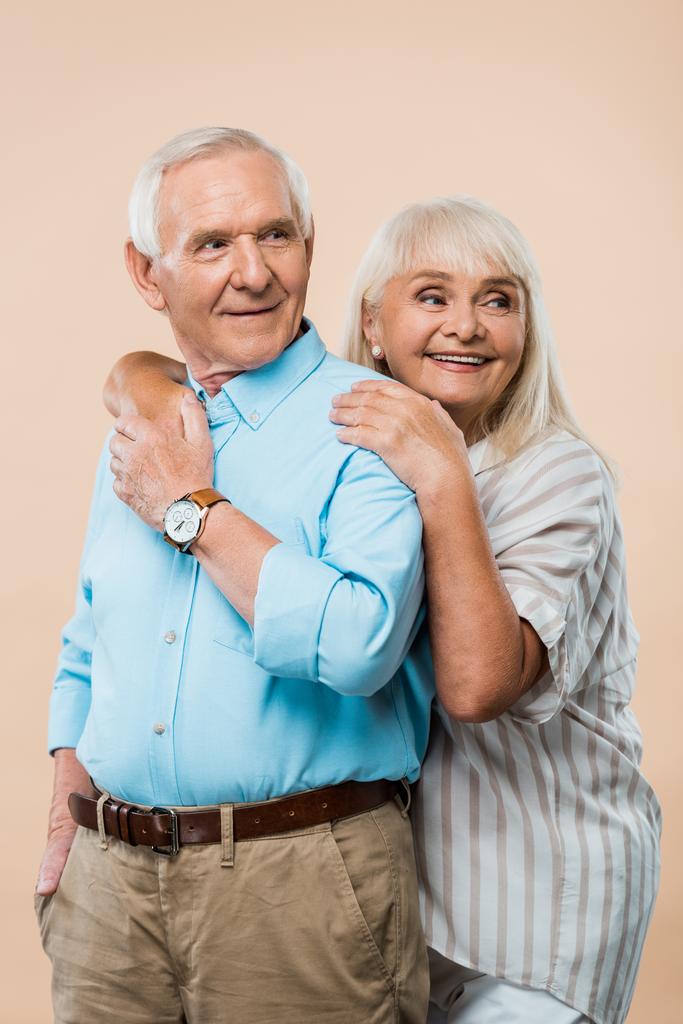 alegre jubilado mujer abrazando marido mientras toma de la mano aislado en beige
  - Foto, Imagen