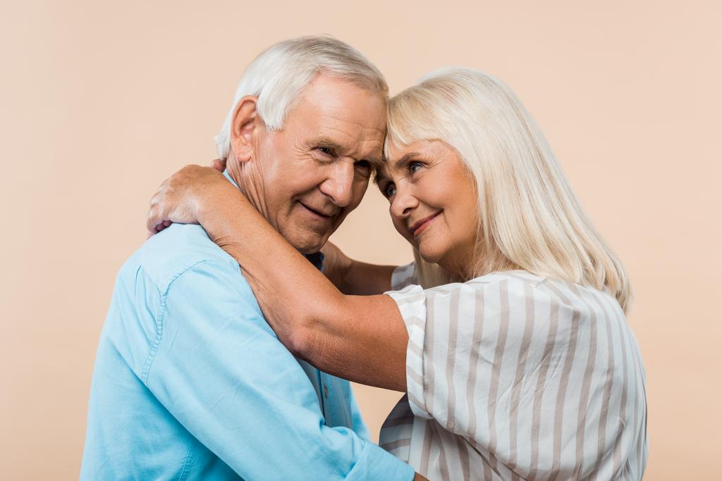 Gelukkig gepensioneerde vrouw kijken naar man met knuffelen geïsoleerd op beige  - Foto, afbeelding