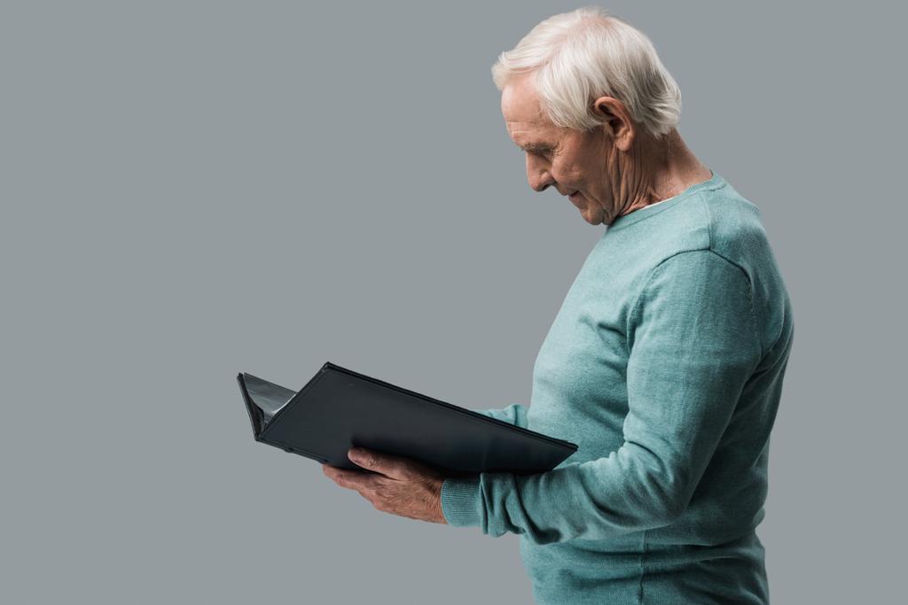 happy retired man with grey hair looking at photo album isolated on grey  - Photo, Image