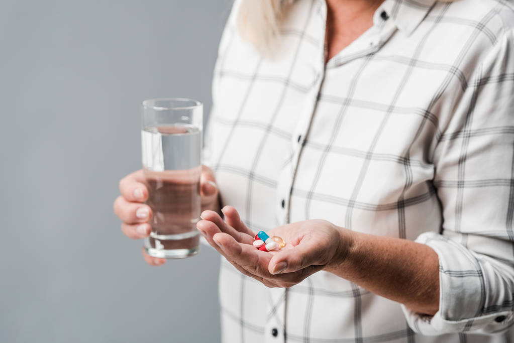 vista recortada de la mujer jubilada sosteniendo pastillas y vaso de agua aislado en gris
  - Foto, imagen