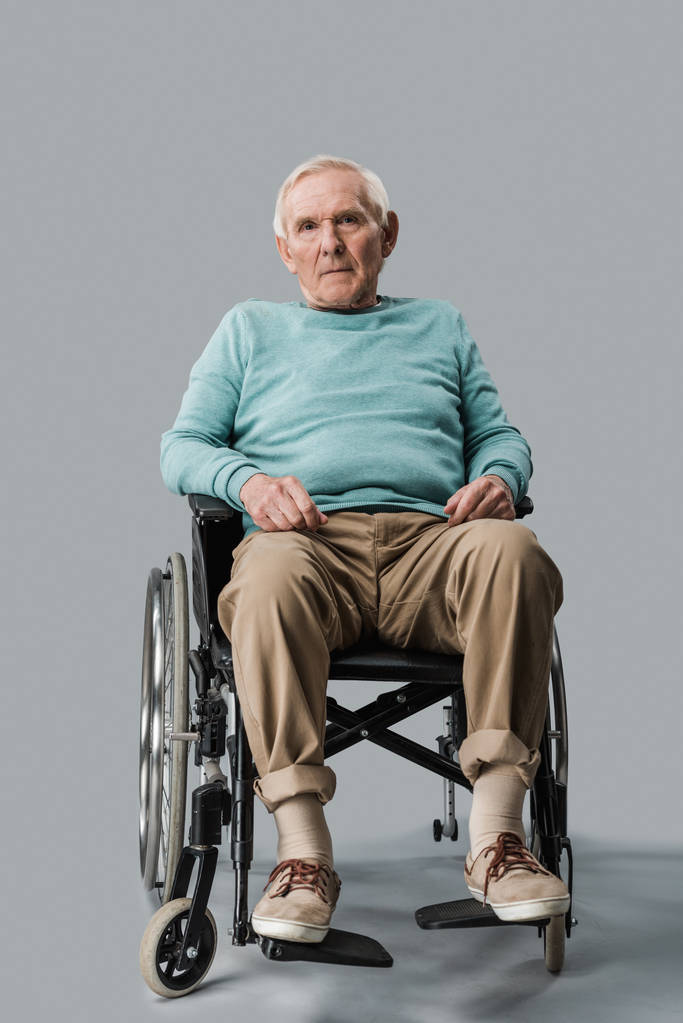 triste uomo anziano seduto sulla sedia a rotelle e guardando la fotocamera su grigio
 - Foto, immagini
