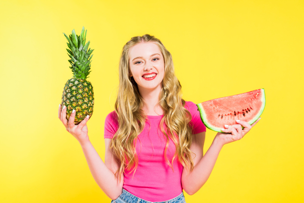 mooi meisje houdt watermeloen en ananas geïsoleerd op geel - Foto, afbeelding