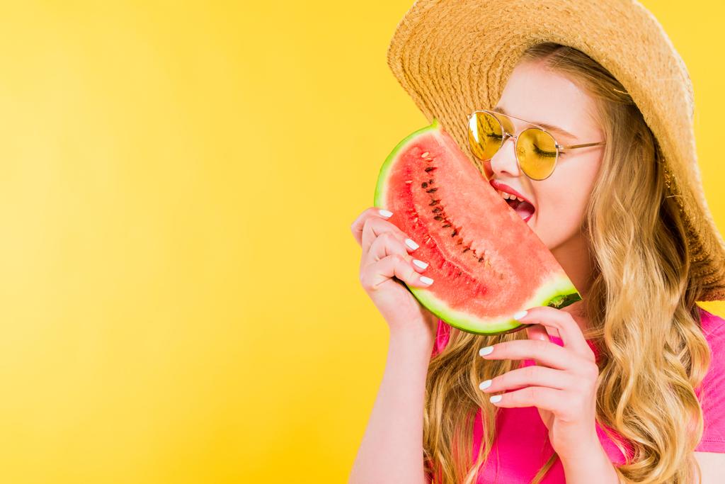 mooi meisje in stro hoed eten watermeloen geïsoleerd op geel - Foto, afbeelding