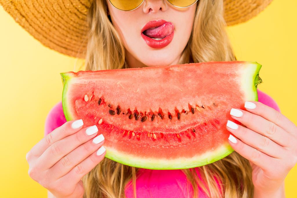 Bijgesneden weergave van meisje tong steken en vasthouden van watermeloen op geel - Foto, afbeelding