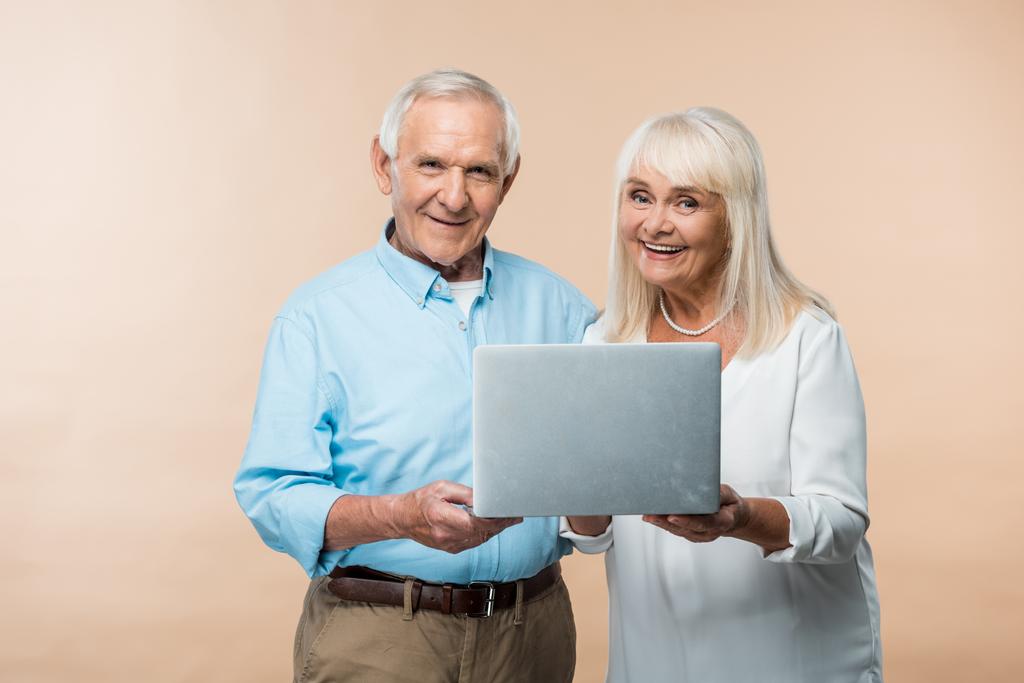 boldog nyugdíjas pár használ laptop és mosolyogva izolált bézs  - Fotó, kép