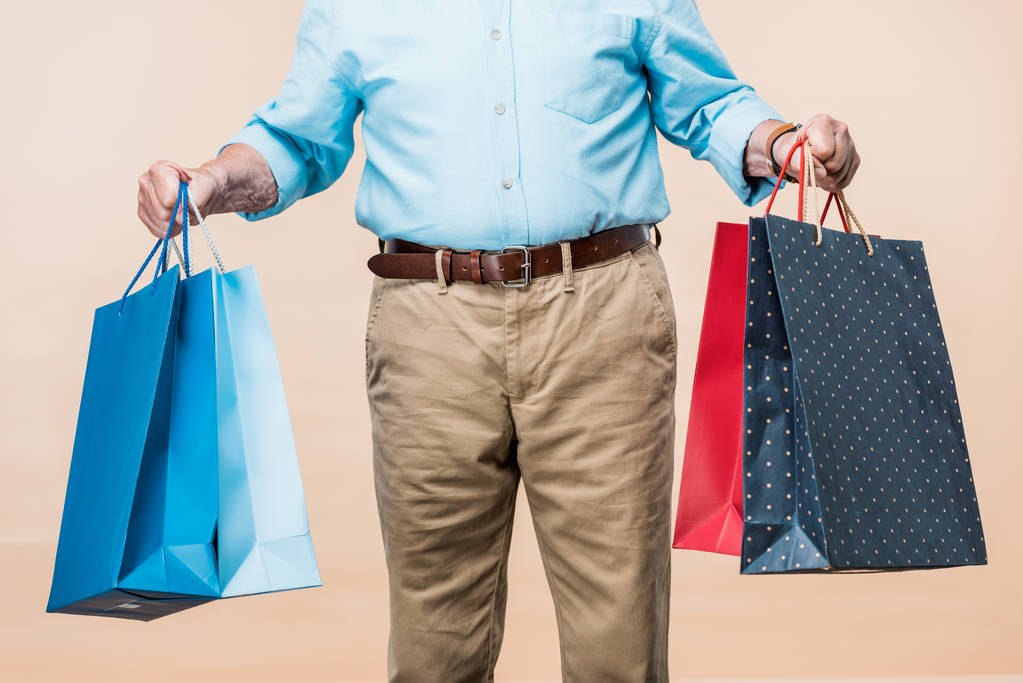 vista cortada de homem aposentado sorrindo segurando sacos de compras isolados em bege
  - Foto, Imagem