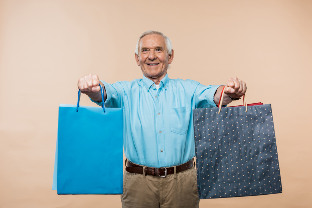 joyeux retraité souriant tout en tenant des sacs à provisions sur beige
  - Photo, image