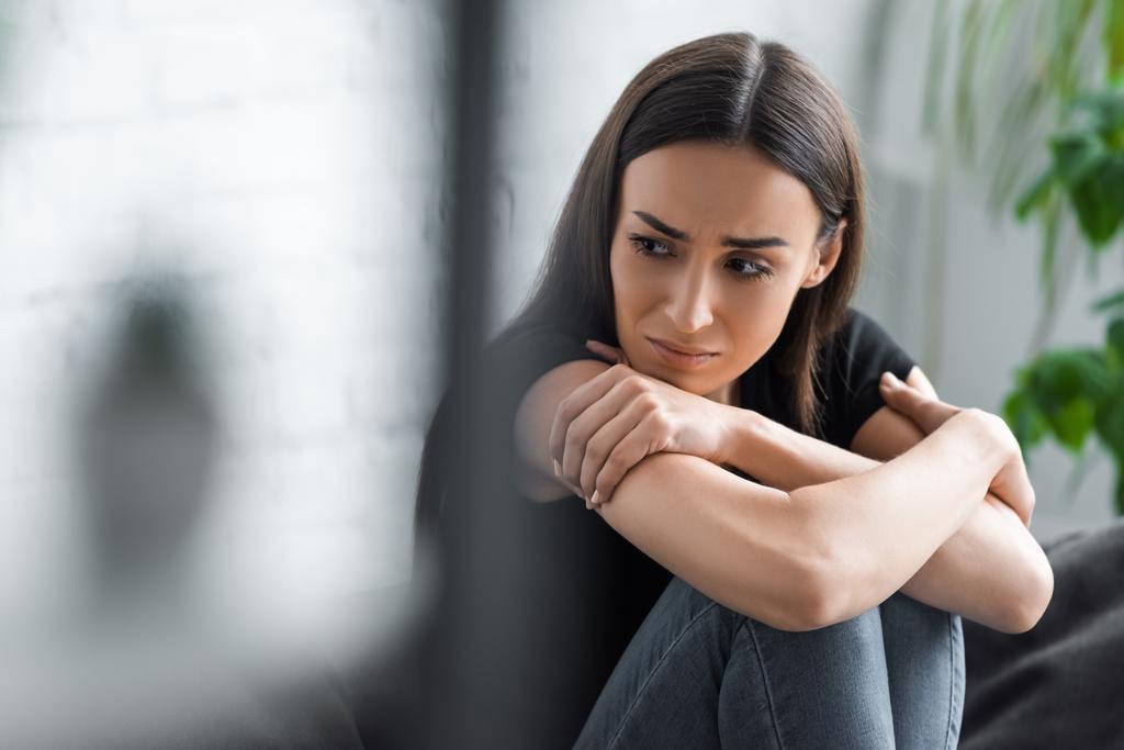 selectieve focus van huilende jonge vrouw die lijdt aan depressie terwijl hij met gekruiste armen zit en wegkijkt - Foto, afbeelding