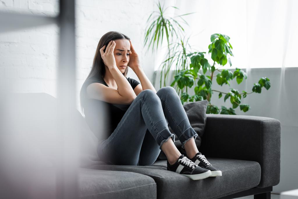 szelektív hangsúlyt a fiatal nő szenved depresszióban, miközben ül a kanapén, és kezében a fej közelében - Fotó, kép