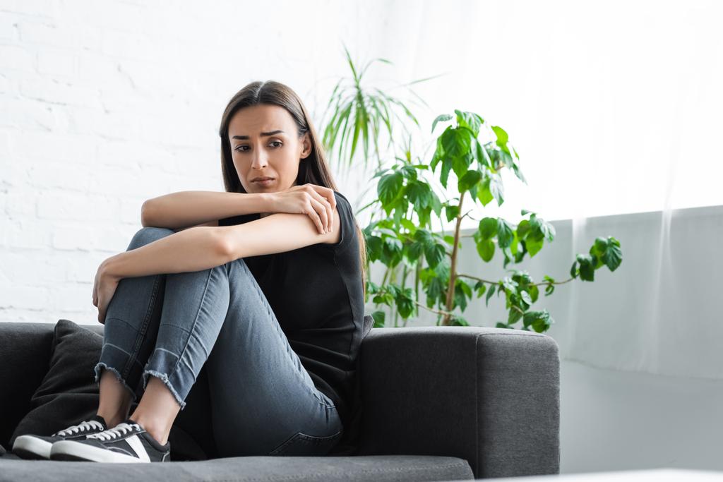 расстроенная молодая женщина страдает от депрессии и плачет, сидя на диване дома
 - Фото, изображение