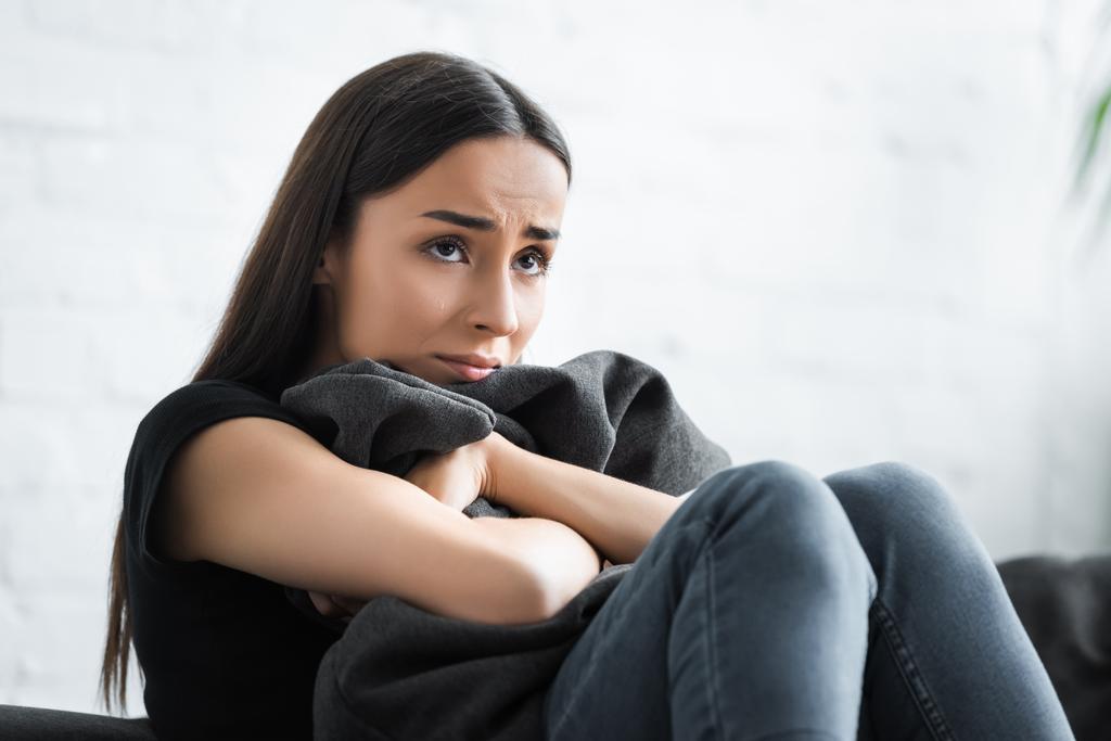 depressive junge Frau umarmt Kissen und schaut weg, während sie zu Hause auf dem Sofa sitzt - Foto, Bild