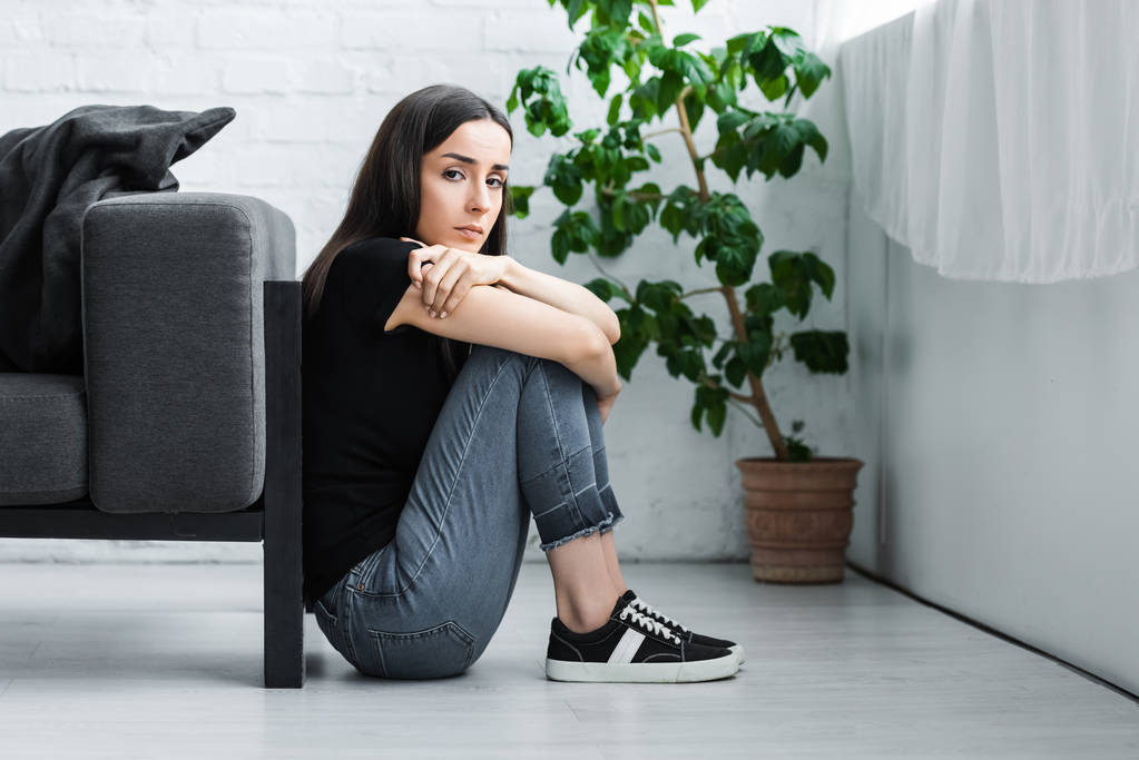 mujer joven deprimida sentada en el suelo en casa y mirando a la cámara
 - Foto, imagen