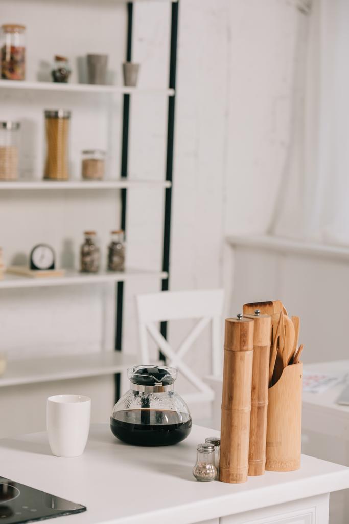 木製のスパイスミルの近くにコーヒーポットとホワイトカップ付きのキッチンテーブル  - 写真・画像