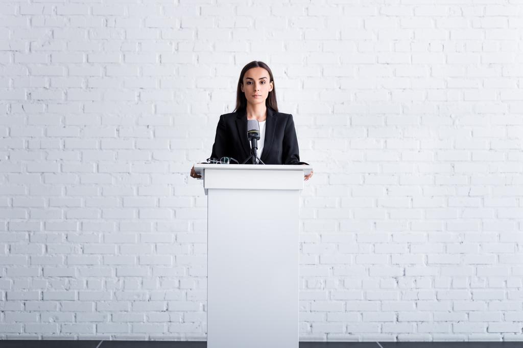 beautiful, confident lecturer standing on podium tribune near white brick wall - Photo, Image