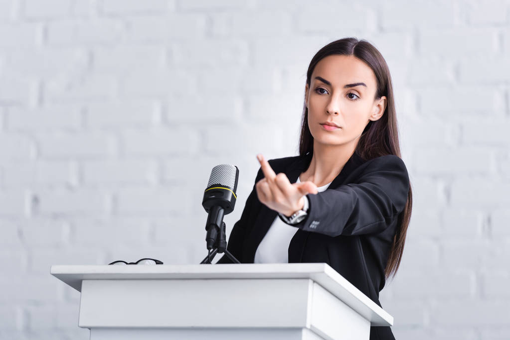 profesor insatisfecho de pie en el tribuno podio en la sala de conferencias y mostrando el dedo medio
 - Foto, imagen