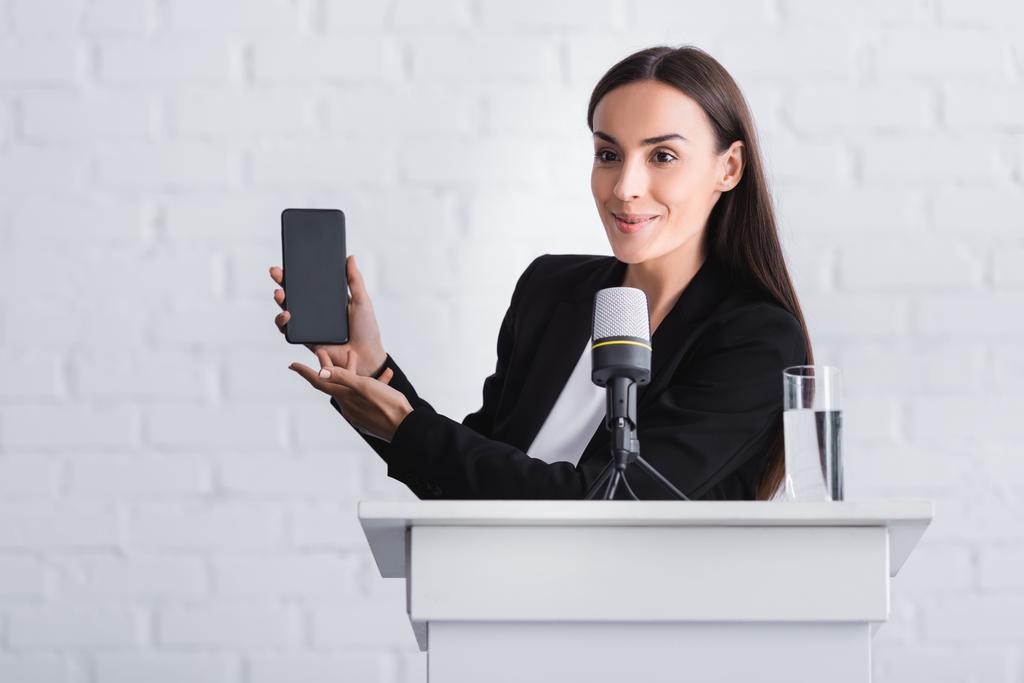 alegre conferenciante de pie en tribuna podio y la presentación de smartphone con pantalla en blanco
 - Foto, imagen