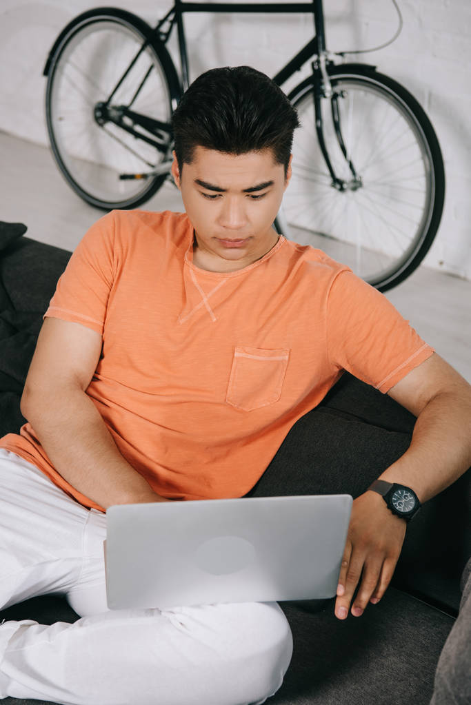 keskittynyt asukas mies käyttää kannettavaa tietokonetta istuessaan sohvalla kotona
 - Valokuva, kuva