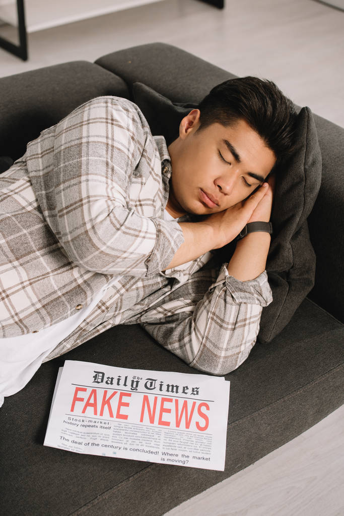 väsynyt aasialainen mies nukkuu sohvalla kotona lähellä sanomalehti fake uutiset
 - Valokuva, kuva