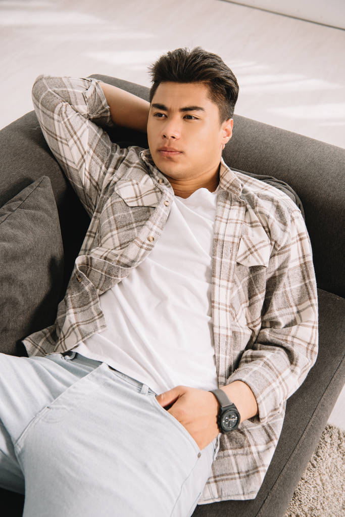 jeune, rêveur asiatique homme regardant loin tandis que couché sur canapé à la maison
 - Photo, image
