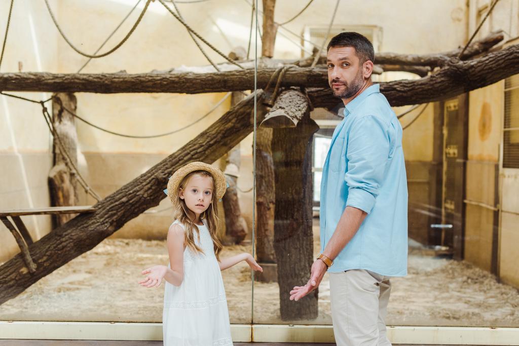 aranyos gyerek és csinos apa mutatja vállrándítással gesztus az állatkertben  - Fotó, kép