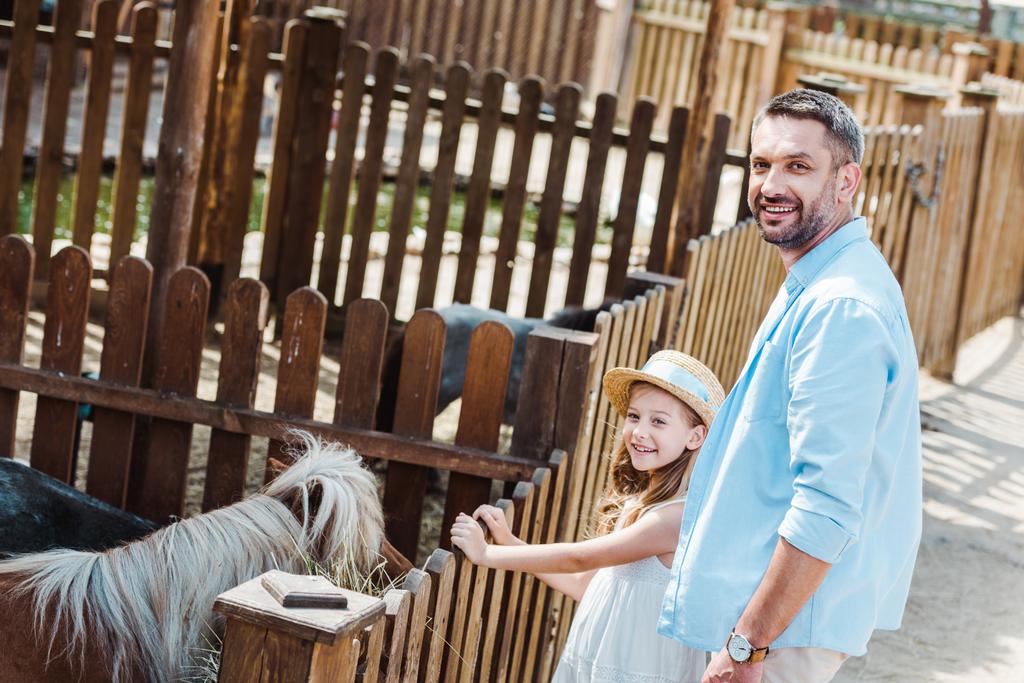fröhliches Kind und Mann lächelnd neben Pony im Zoo  - Foto, Bild