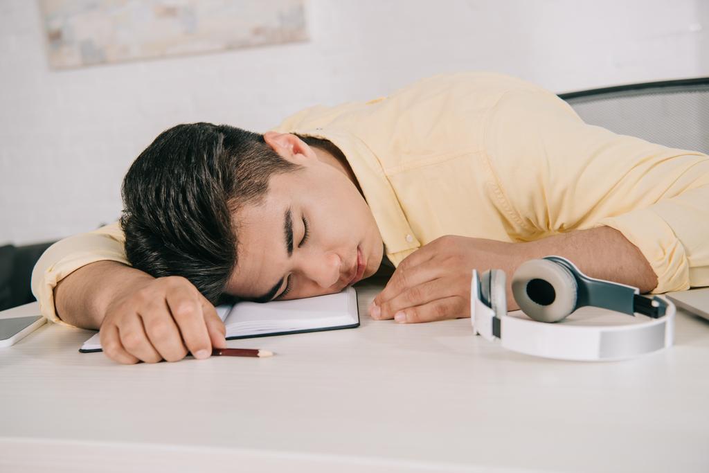 exhausted young man sleeping while sitting at table and holding pencil - Photo, Image