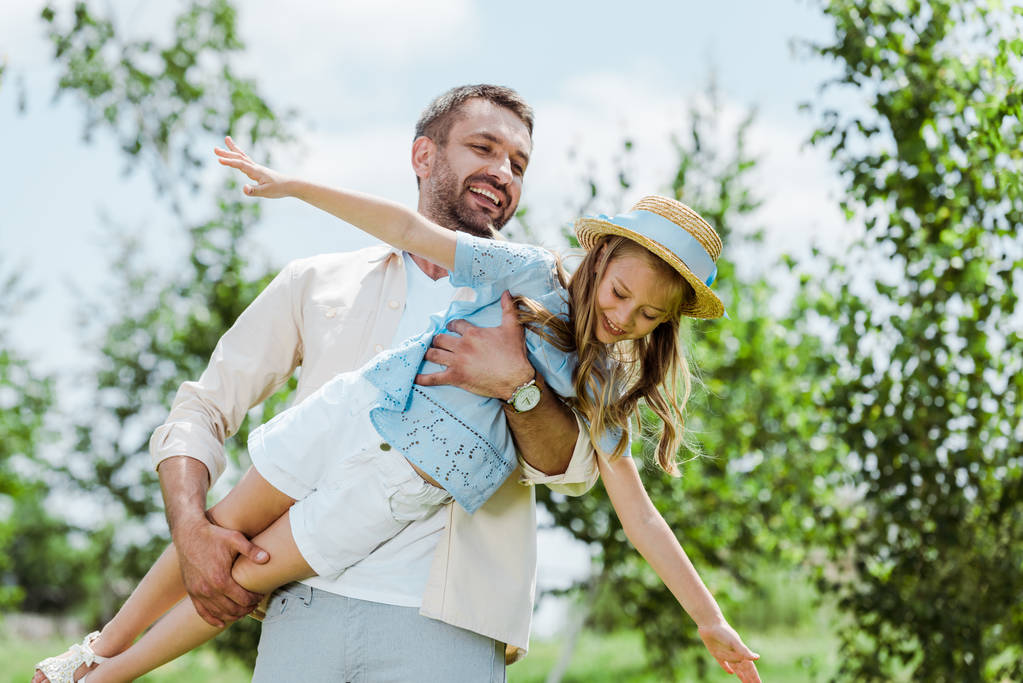 alegre padre sosteniendo en brazos feliz hija en paja sombrero
  - Foto, imagen
