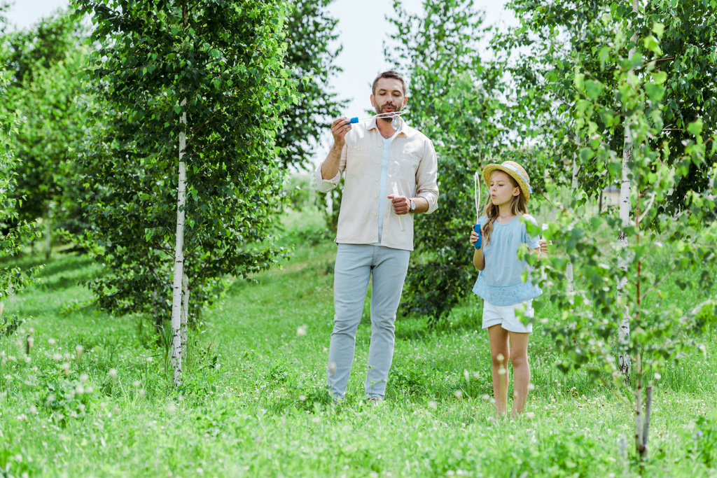 enfoque selectivo de padre e hija soplando burbujas de jabón cerca de los árboles
 - Foto, Imagen