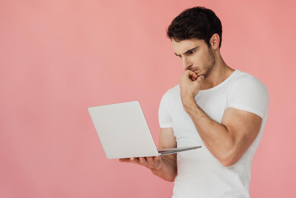 zamyślony muskularny Człowiek w białym t-shirt za pomocą laptopa izolowane na różowy - Zdjęcie, obraz