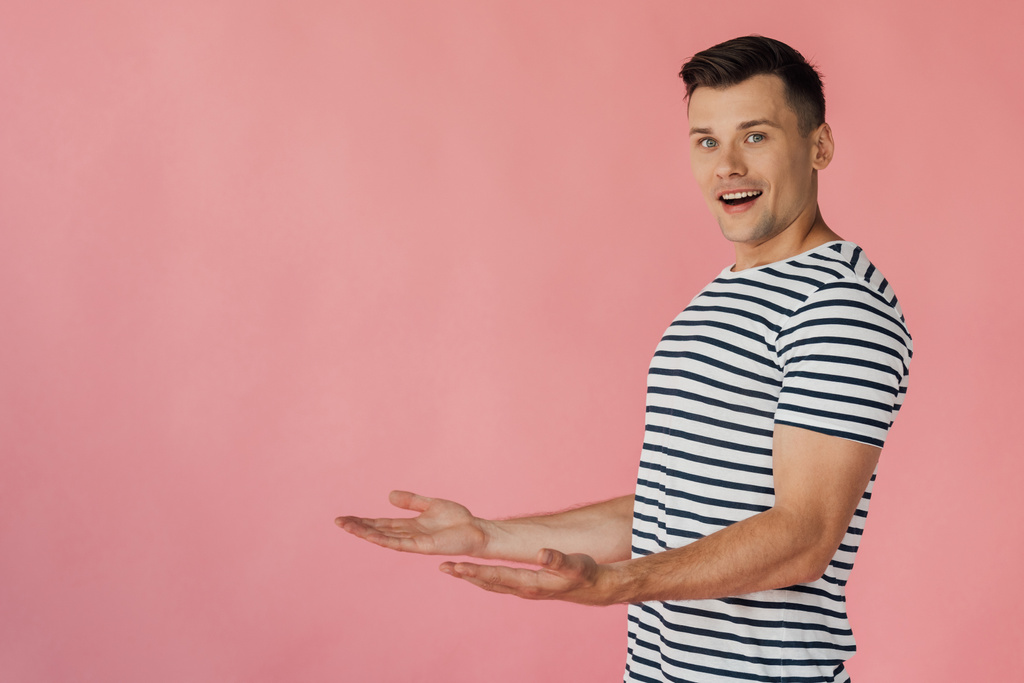 hymyilevä mies raidallinen t-paita osoittaa kädet eristetty vaaleanpunainen
 - Valokuva, kuva
