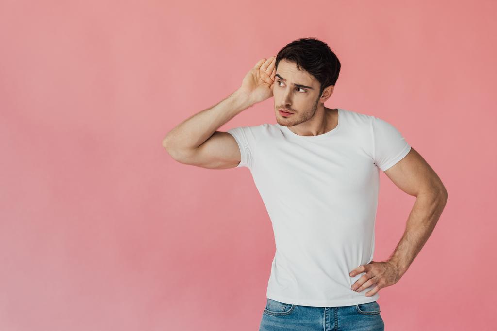 muskulöser Mann in weißem T-Shirt, Handfläche am Ohr haltend und isoliert auf rosa - Foto, Bild