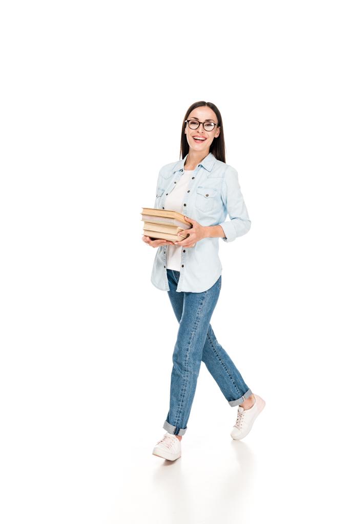 szczęśliwy brunetka dziewczyna w okularach w kurtka dżinsowa chodzenie z książek na białym tle - Zdjęcie, obraz