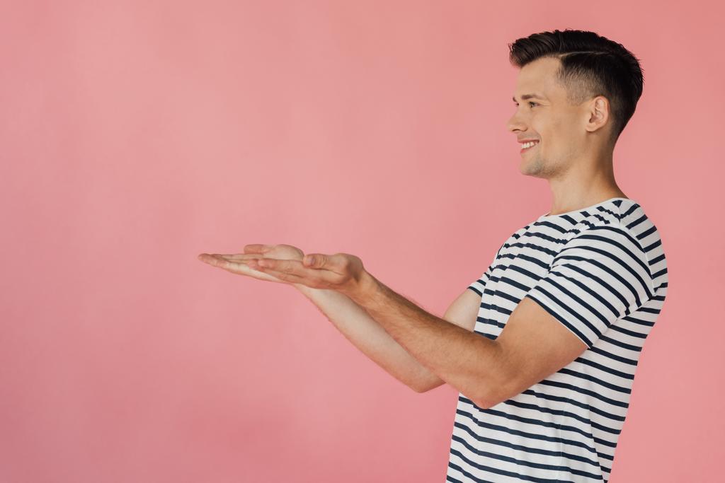 smiling man in striped t-shirt pointing with hands isolated on pink - Photo, Image