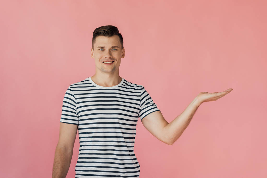 front view of smiling man in striped t-shirt pointing with hand isolated on pink - Photo, Image