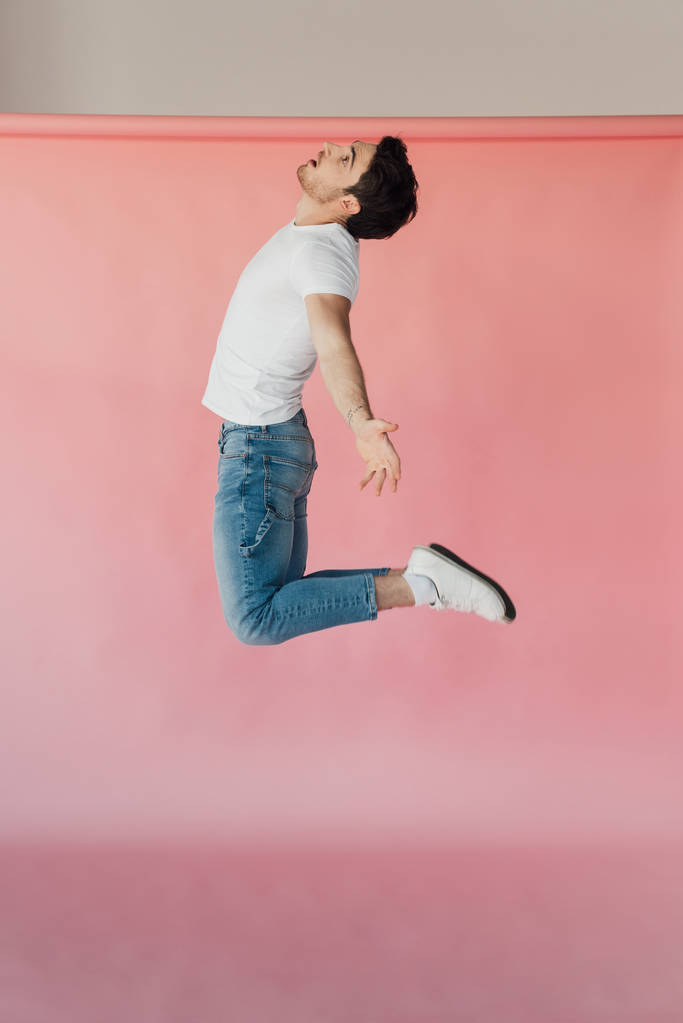мускулистый мужчина в белой футболке и джинсах, прыгающий на розовом
 - Фото, изображение