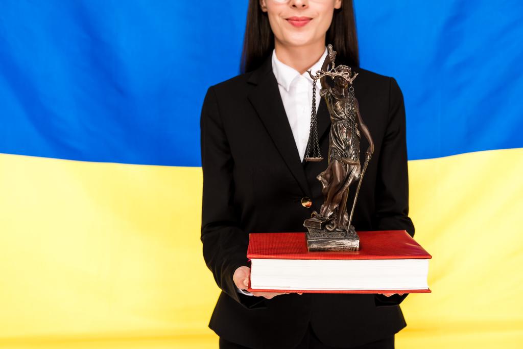 vista ritagliata di avvocato in tuta nera che tiene Themis figurina sul libro su sfondo bandiera ucraina
 - Foto, immagini