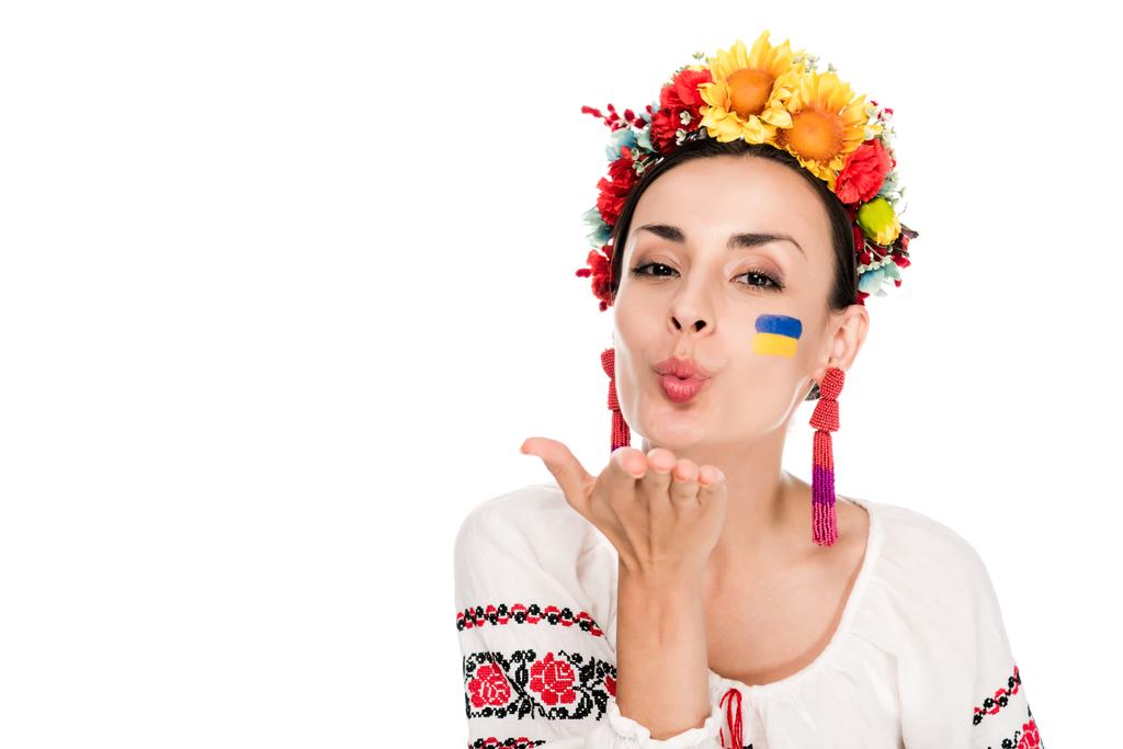 brunetka młoda kobieta w krajowych ukraińskich haftowane koszula i kwiatowy wieniec dmuchanie pocałunek na białym tle - Zdjęcie, obraz