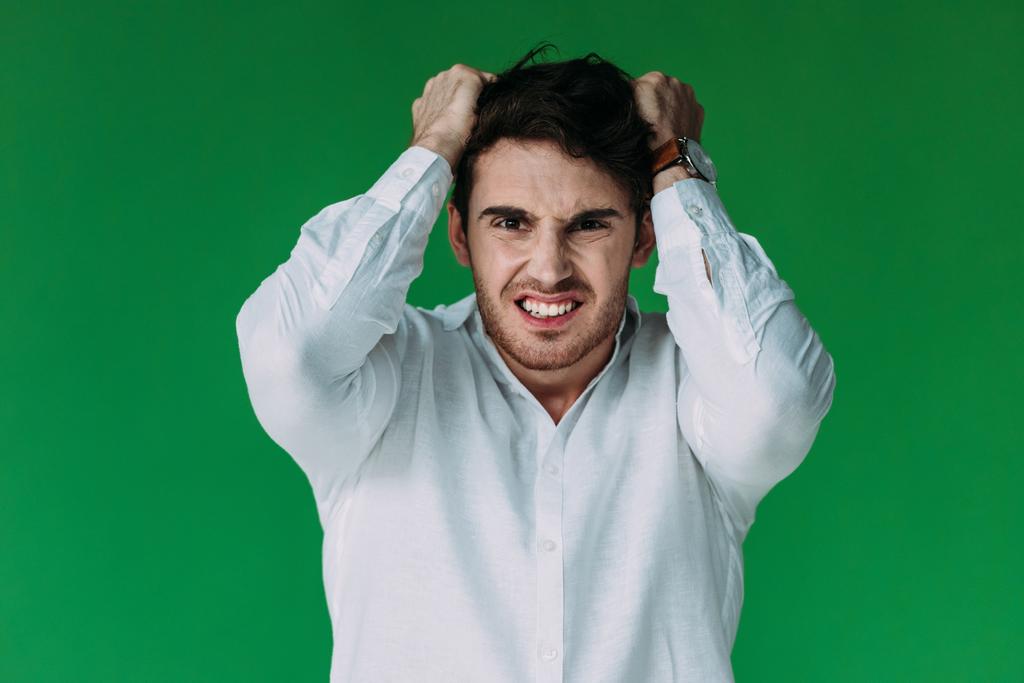 front view of angry man in white shirt looking at camera isolated on green - Photo, Image