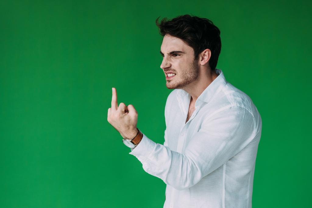 Wütender Mann im weißen Hemd schaut weg und zeigt Mittelfinger isoliert auf grün - Foto, Bild