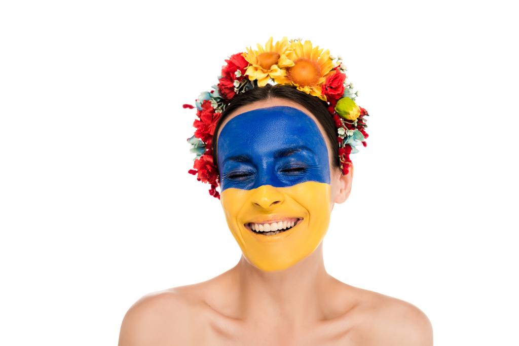 mujer joven desnuda en corona floral con bandera ucraniana pintada en la piel sonriendo con los ojos cerrados aislados en blanco
 - Foto, Imagen