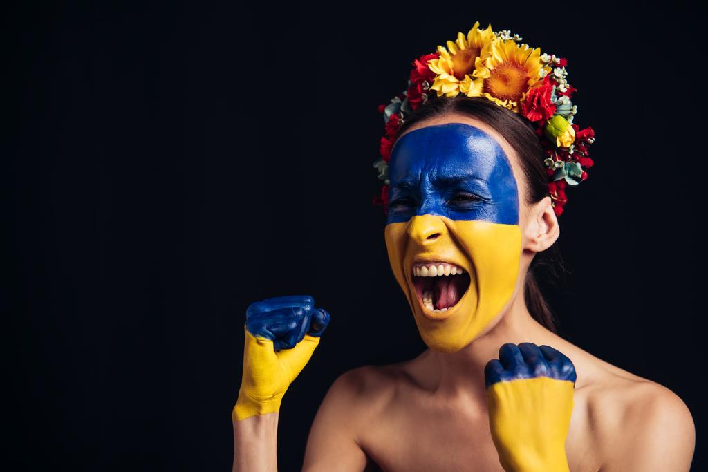 naakte jonge vrouw in bloemen krans met geschilderde Oekraïense vlag op de huid schreeuwen en doen ja gebaar geïsoleerd op zwart - Foto, afbeelding