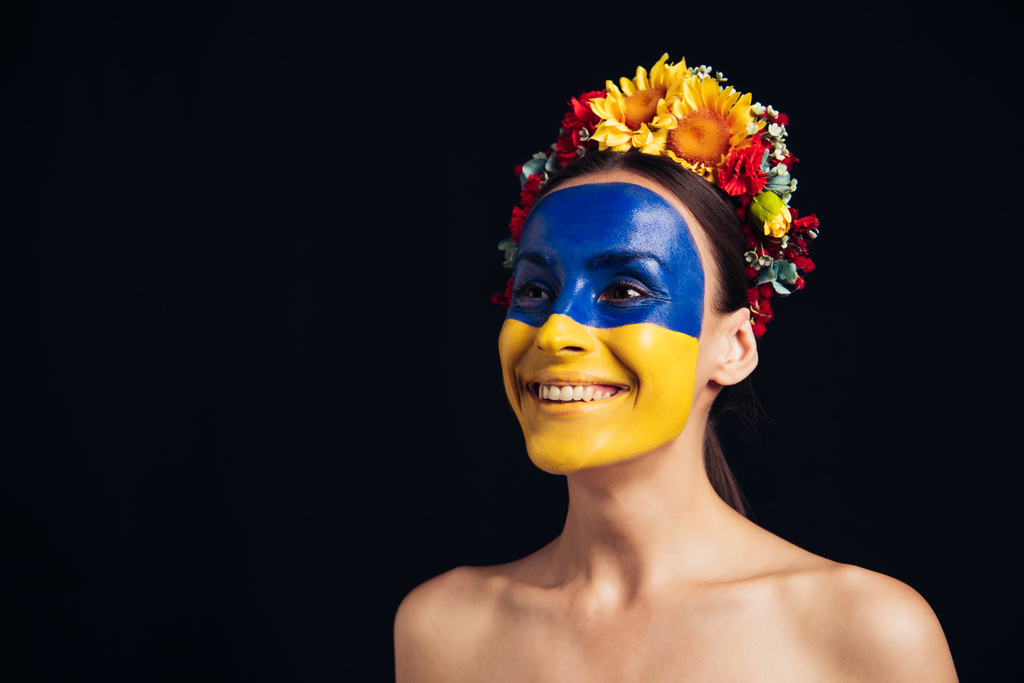 щаслива гола молода жінка в квітковому Вінці з намальованим українським прапором на шкірі, ізольованому на чорному - Фото, зображення
