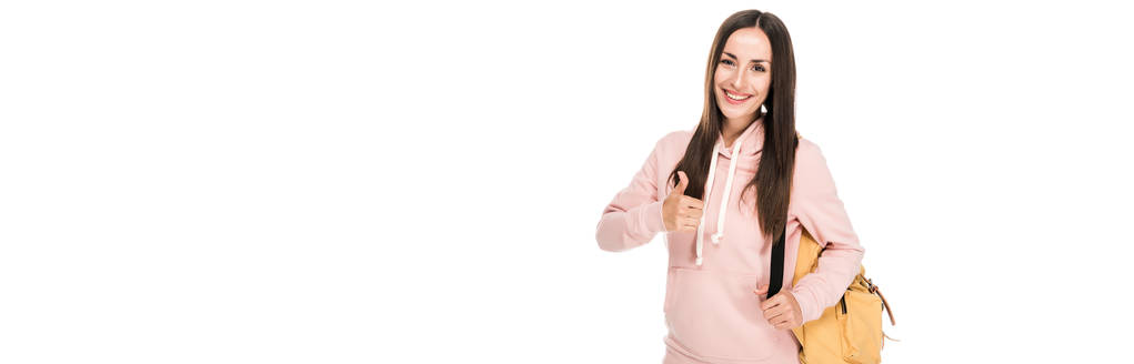 glimlachend brunette meisje met rugzak weergegeven duim omhoog geïsoleerd op wit, panoramisch schot - Foto, afbeelding